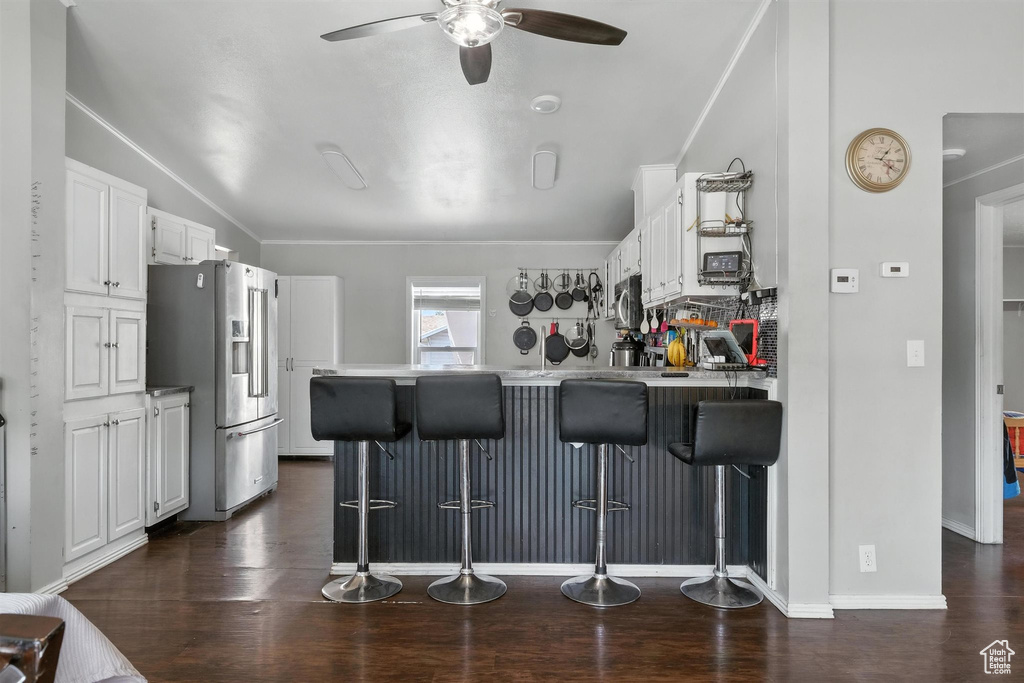 Kitchen with appliances with stainless steel finishes, a peninsula, a ceiling fan, white cabinetry, and crown molding