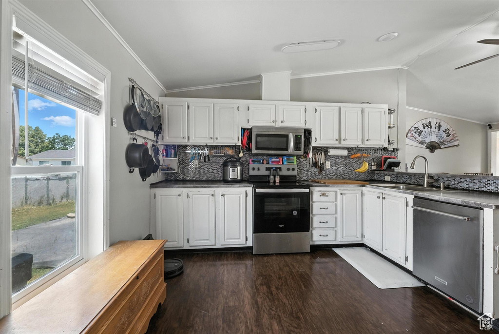 Kitchen featuring appliances with stainless steel finishes, vaulted ceiling, ornamental molding, decorative backsplash, and dark wood-style flooring