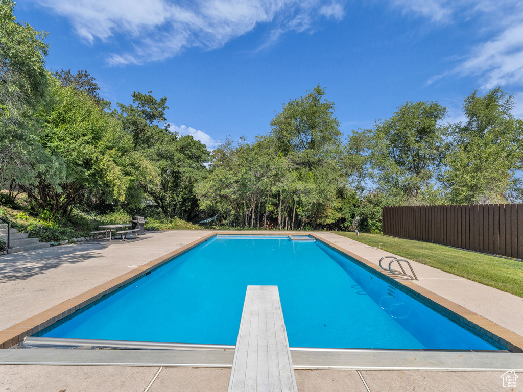 View of swimming pool featuring a patio area, a diving board, and view of wooded area