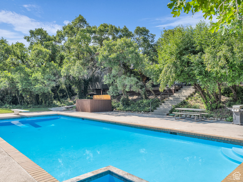 Swimming pool with stairway, a grill, view of scattered trees, and a diving board