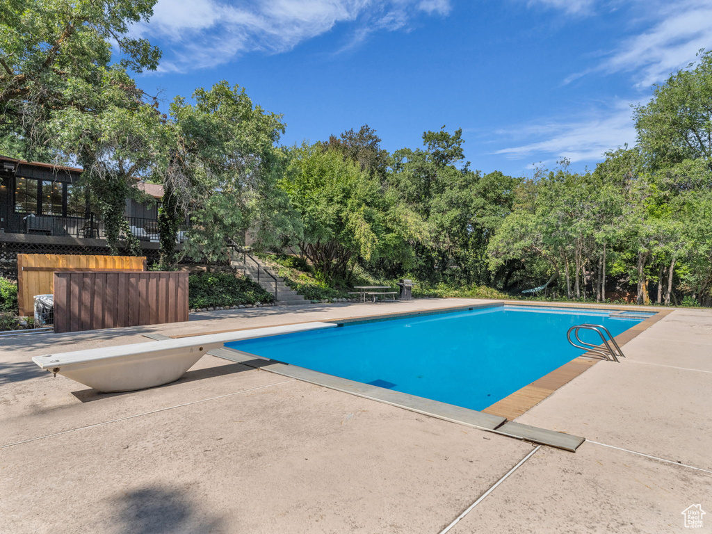Outdoor pool featuring a diving board, a patio, and view of wooded area