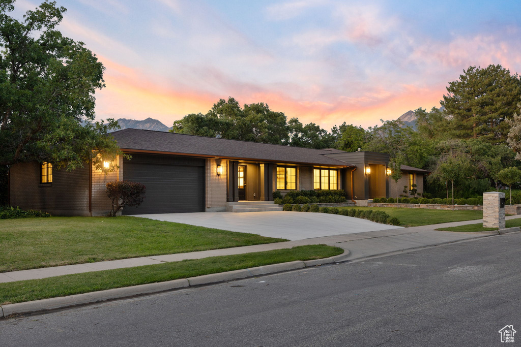 View of front of house with concrete driveway, a garage, a yard, and brick siding