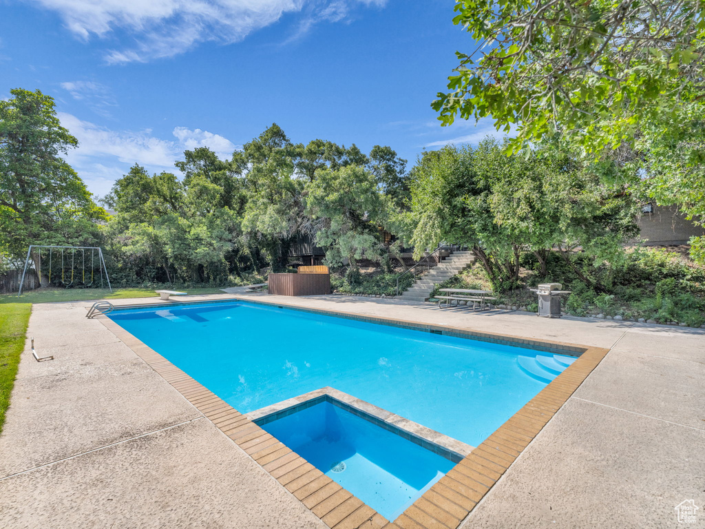 View of pool with view of wooded area, stairs, a patio area, a pool with connected hot tub, and a diving board