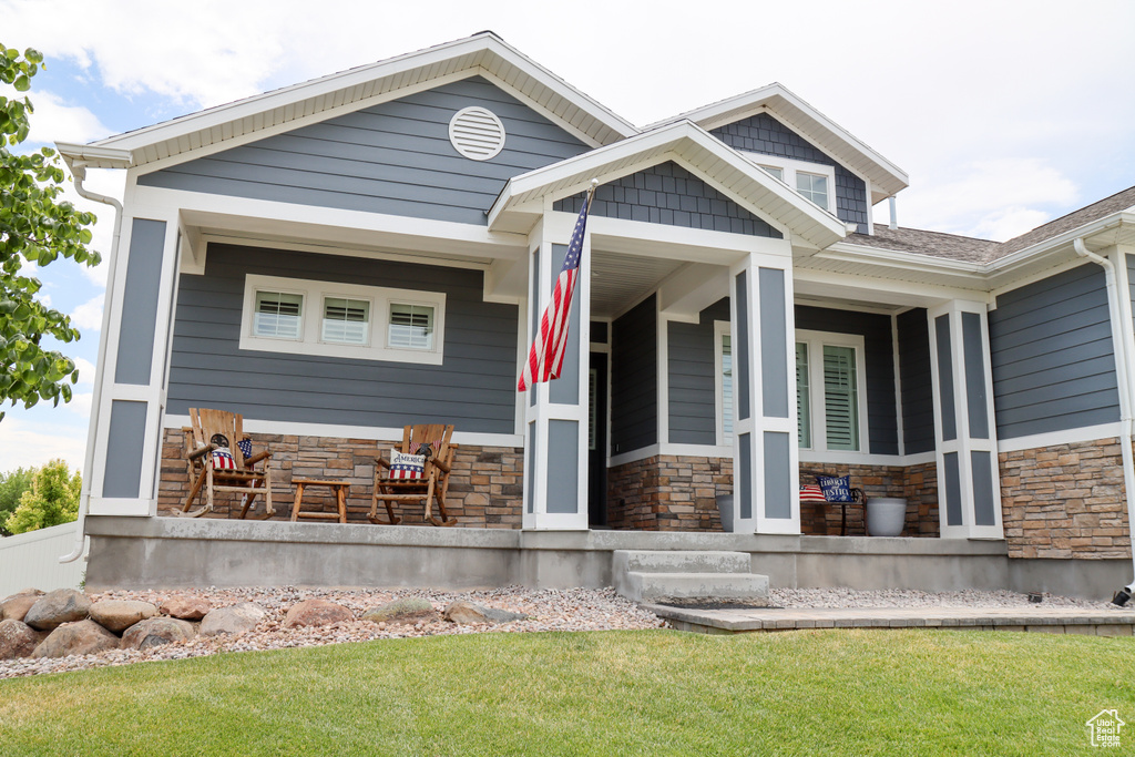 View of front facade with stone siding, a porch, and a front lawn