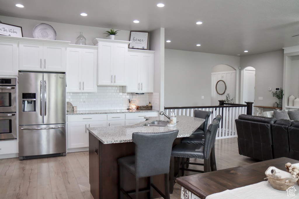 Kitchen featuring stainless steel appliances, arched walkways, white cabinetry, backsplash, and light wood-style flooring