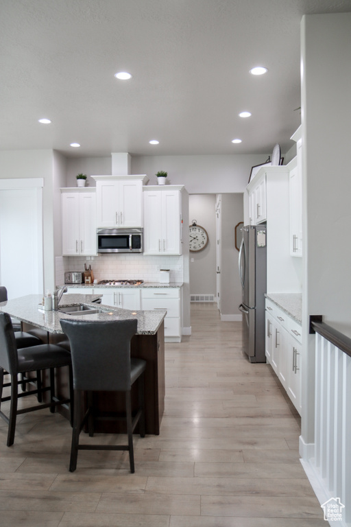 Kitchen featuring stainless steel appliances, a kitchen bar, white cabinets, and recessed lighting