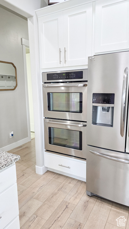 Kitchen with appliances with stainless steel finishes, light wood-type flooring, white cabinets, and light countertops