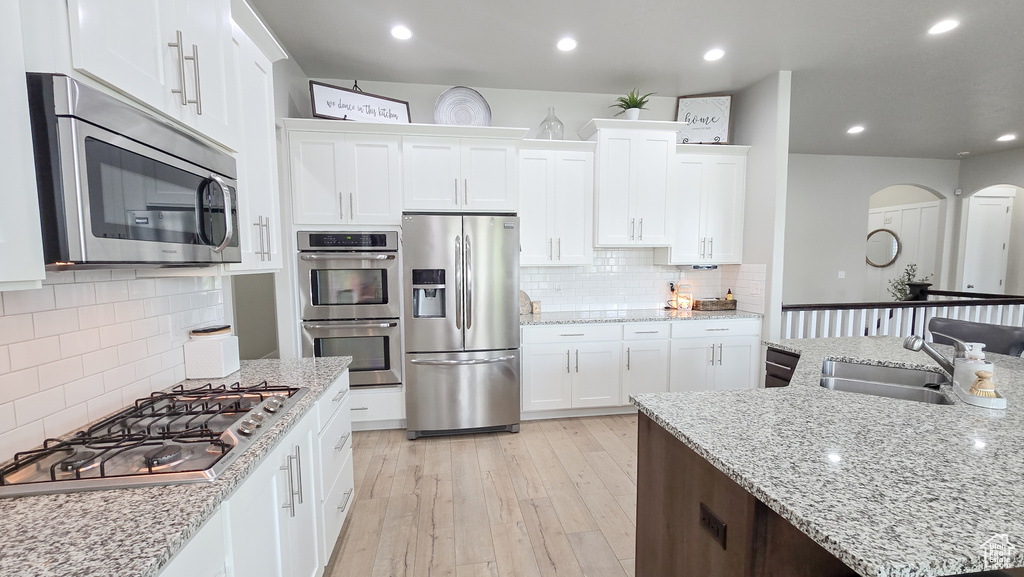 Kitchen featuring stainless steel appliances, backsplash, arched walkways, white cabinets, and recessed lighting