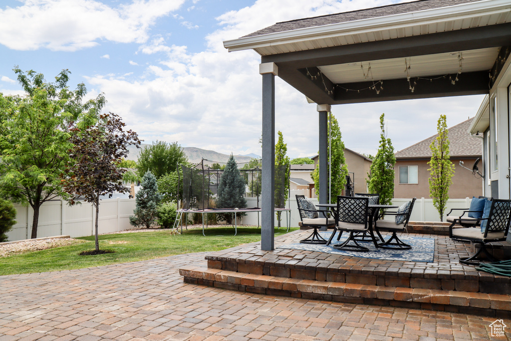 Fenced backyard with a trampoline, a patio area, outdoor dining area, and a mountain view