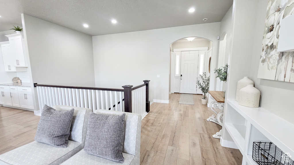 Hallway with light wood-style flooring, arched walkways, and recessed lighting