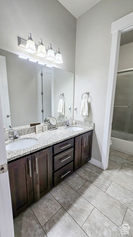 Full bath featuring double vanity, enclosed tub / shower combo, and tile patterned flooring