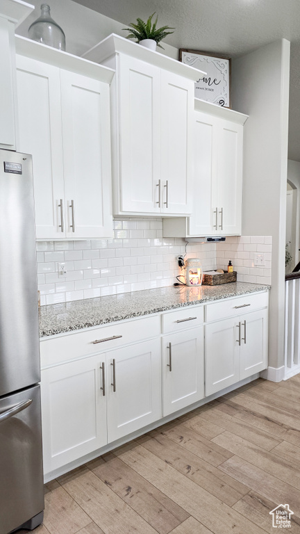 Kitchen with freestanding refrigerator, light wood-style floors, white cabinetry, backsplash, and light stone counters