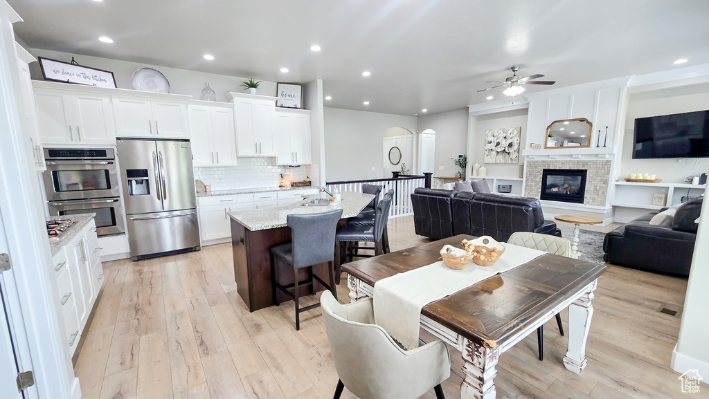 Dining room featuring arched walkways, a ceiling fan, light wood-type flooring, a glass covered fireplace, and recessed lighting