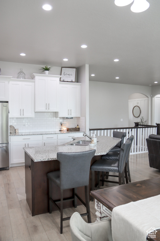 Kitchen with freestanding refrigerator, a breakfast bar, white cabinets, a center island with sink, and light stone countertops