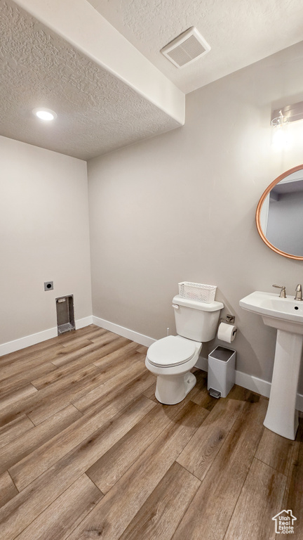 Bathroom with a textured ceiling, wood finished floors, and recessed lighting