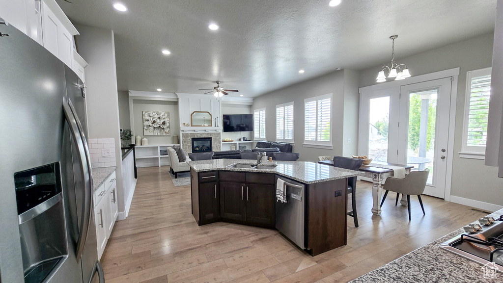 Kitchen featuring appliances with stainless steel finishes, a glass covered fireplace, dark brown cabinetry, recessed lighting, and light wood-type flooring