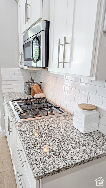 Kitchen with appliances with stainless steel finishes, white cabinetry, light stone countertops, and decorative backsplash