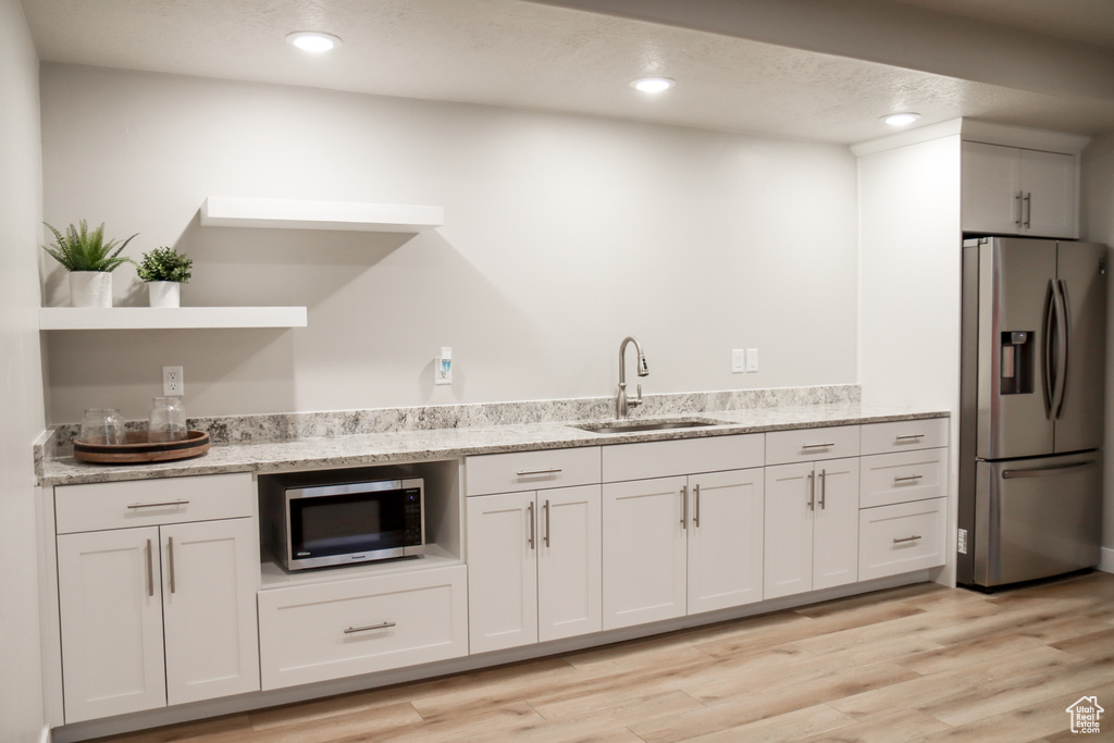 Kitchen featuring stainless steel appliances, open shelves, light wood-style flooring, recessed lighting, and light stone counters