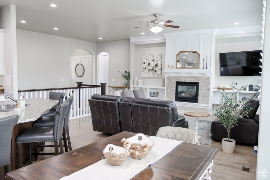 Dining area featuring arched walkways, ceiling fan, recessed lighting, wood finished floors, and a glass covered fireplace