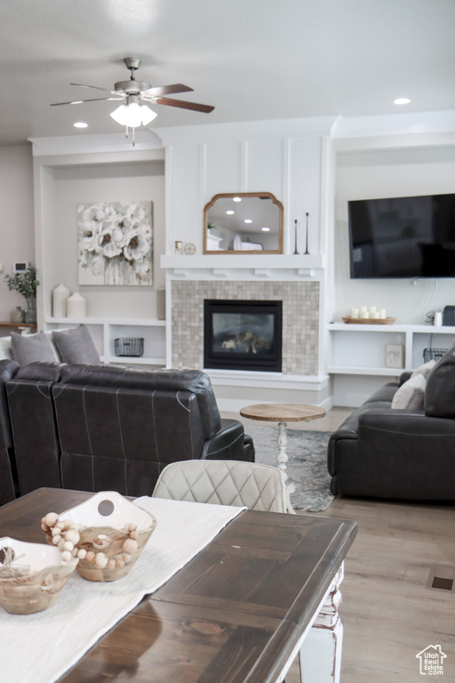 Living area featuring light wood-style floors, ceiling fan, a tiled fireplace, recessed lighting, and built in shelves