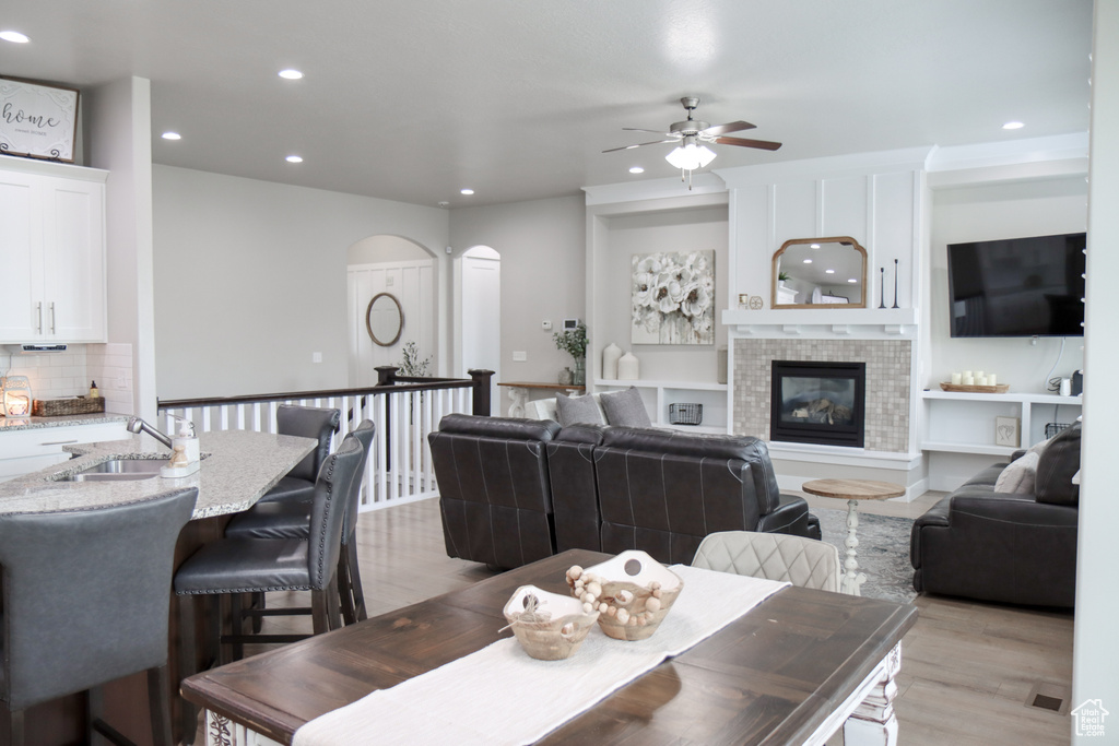 Dining space with arched walkways, recessed lighting, ceiling fan, light wood-style floors, and a tiled fireplace