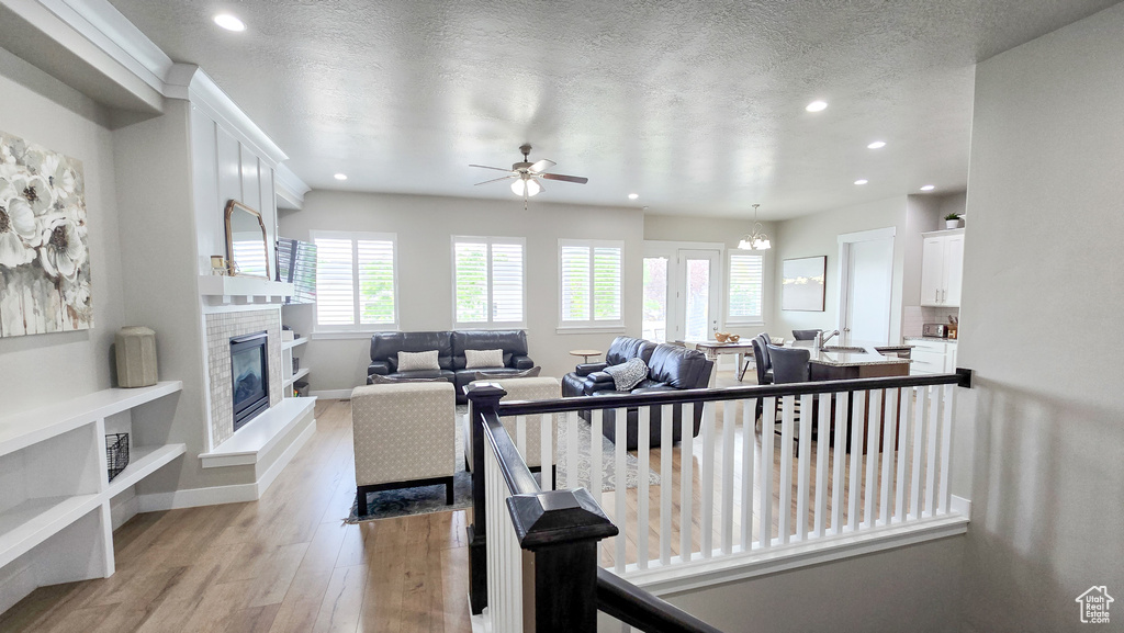 Living area featuring a glass covered fireplace, recessed lighting, light wood-type flooring, ceiling fan, and a chandelier
