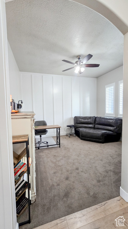 Living area with arched walkways, a decorative wall, a textured ceiling, ceiling fan, and carpet floors