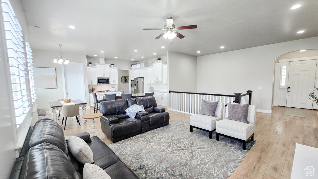 Living room with a ceiling fan, light wood-style flooring, recessed lighting, arched walkways, and a chandelier