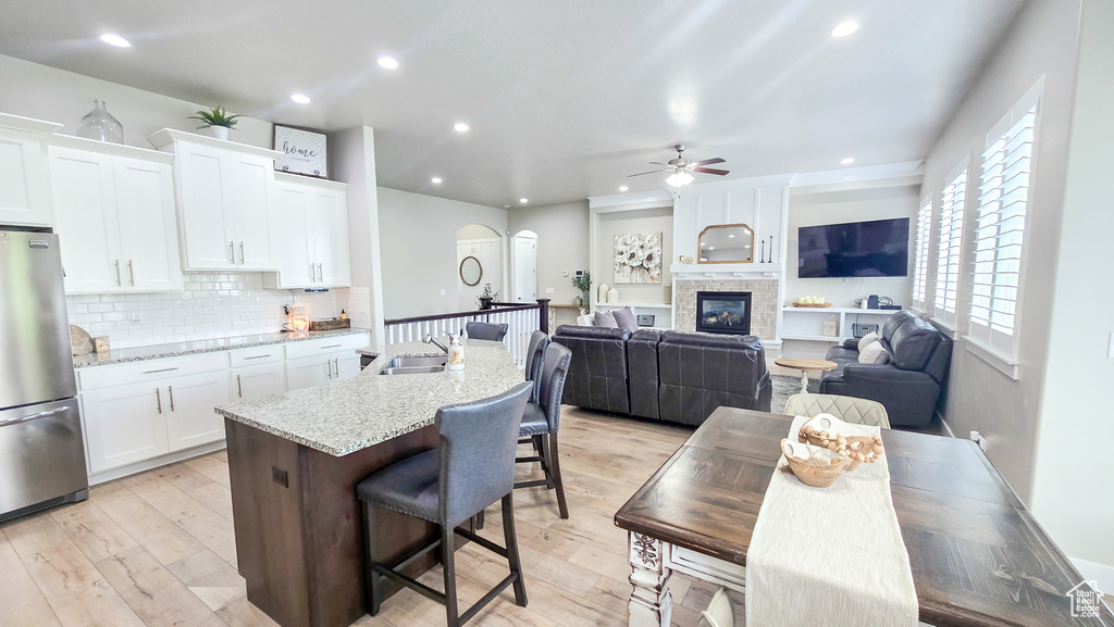 Kitchen with freestanding refrigerator, ceiling fan, a kitchen island with sink, white cabinetry, and a breakfast bar