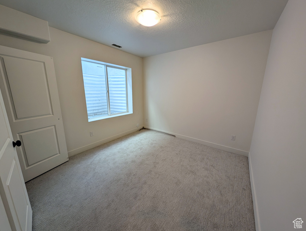 Carpeted spare room with a textured ceiling and baseboards