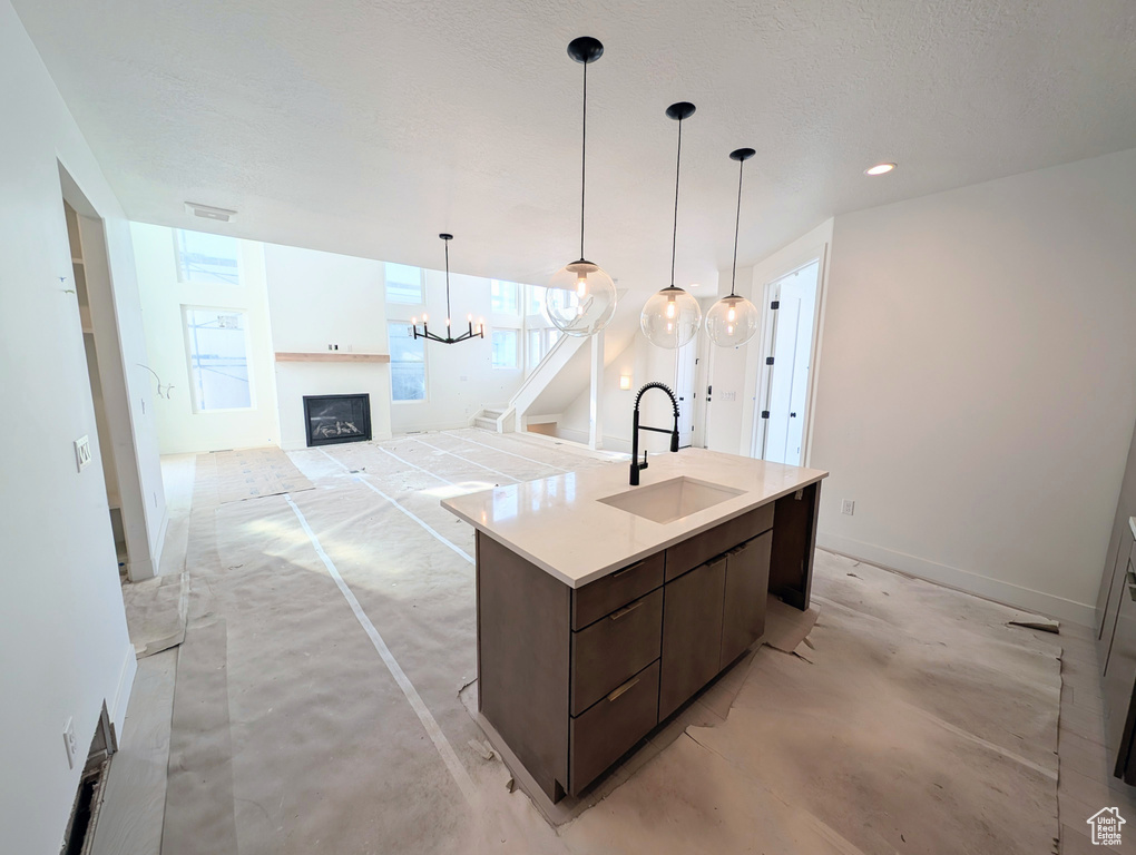 Kitchen with a fireplace, dark brown cabinetry, concrete floors, light countertops, and a kitchen island with sink
