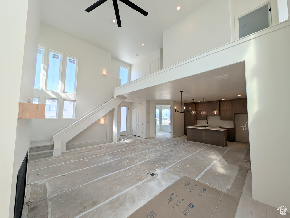 Unfurnished living room with a towering ceiling, stairs, ceiling fan, a chandelier, and recessed lighting