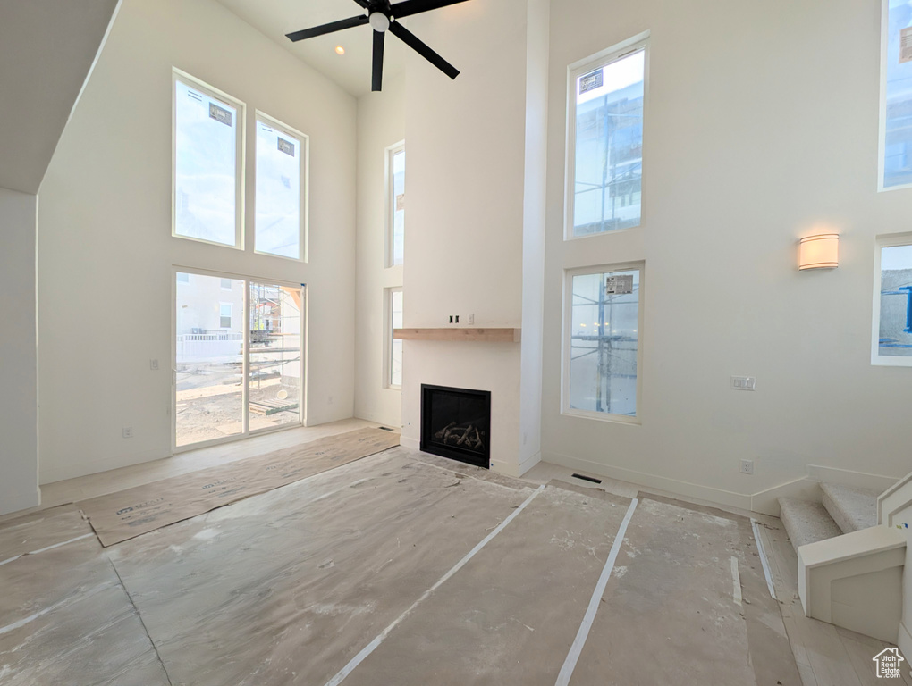 Unfurnished living room featuring a towering ceiling, a fireplace, and ceiling fan
