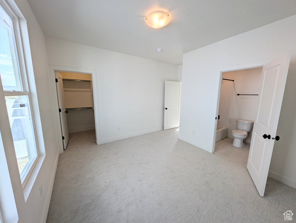 Unfurnished bedroom with light carpet, a walk in closet, ensuite bathroom, and a closet