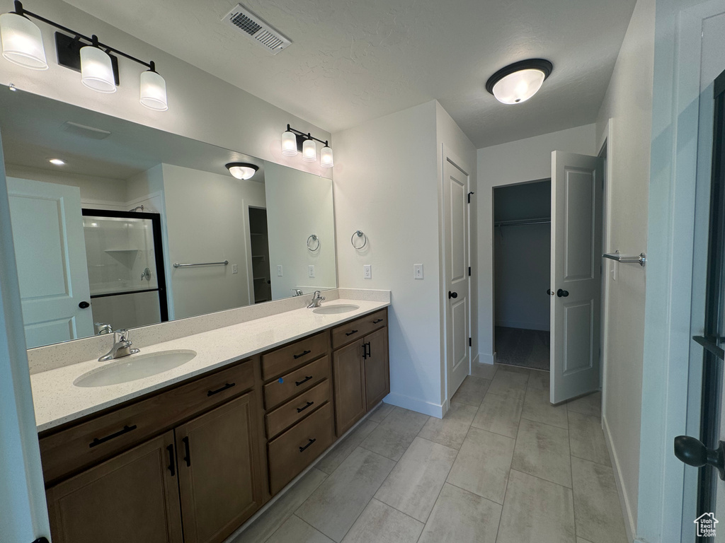 Bathroom with a walk in closet, double vanity, and a stall shower