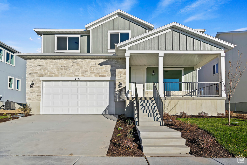View of front of house with stone siding, covered porch, board and batten siding, and concrete driveway