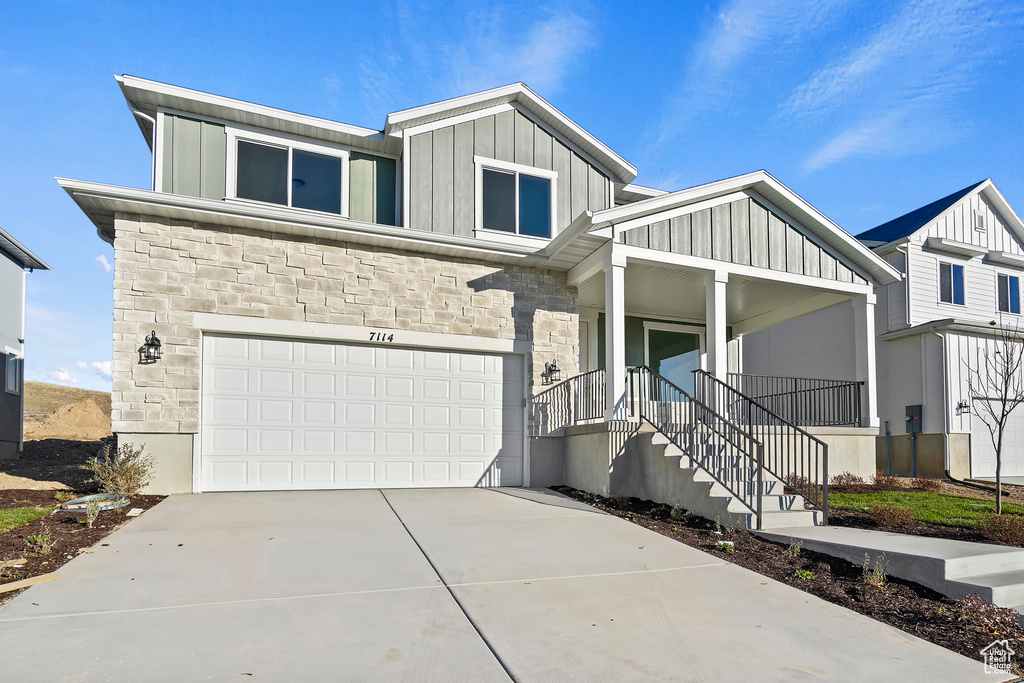 View of front facade featuring board and batten siding, stone siding, covered porch, an attached garage, and driveway
