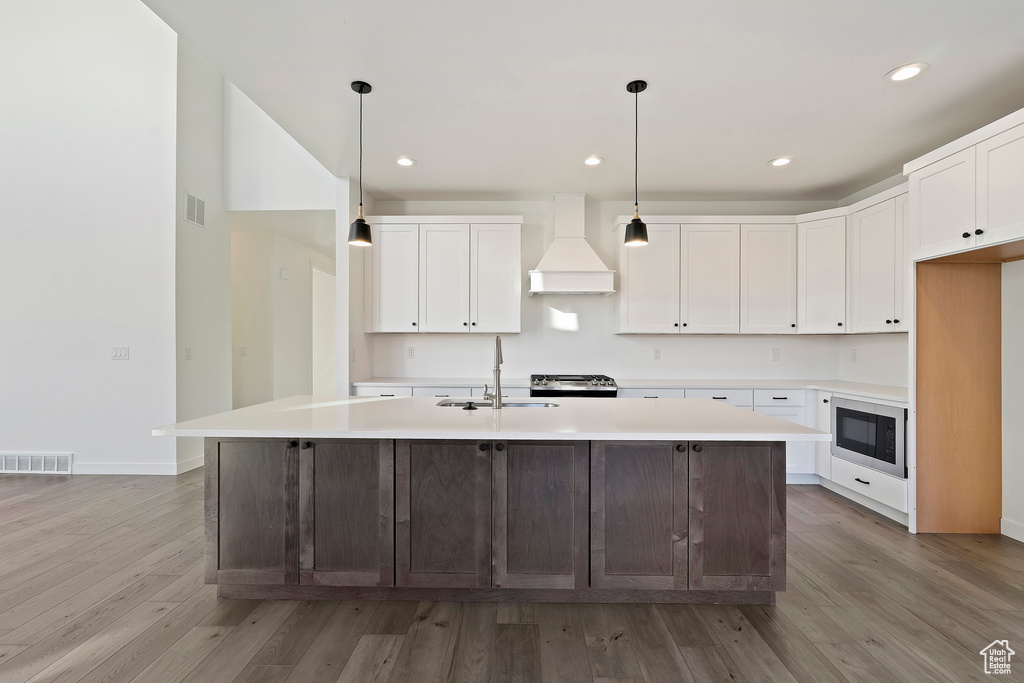 Kitchen with premium range hood, built in microwave, light wood-style floors, light countertops, and recessed lighting