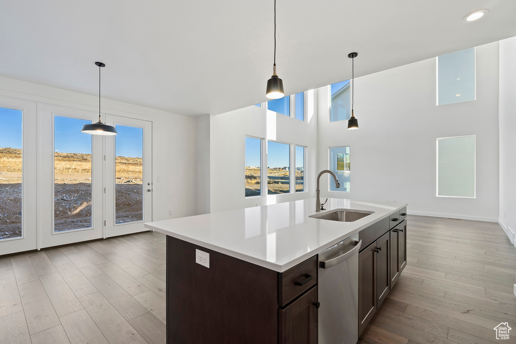 Kitchen featuring stainless steel dishwasher, dark brown cabinets, light countertops, wood finished floors, and decorative light fixtures