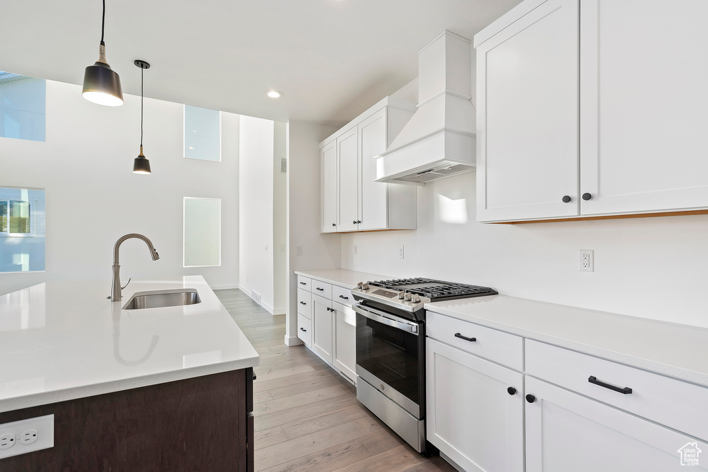 Kitchen featuring gas range, custom exhaust hood, light countertops, light wood-type flooring, and hanging light fixtures