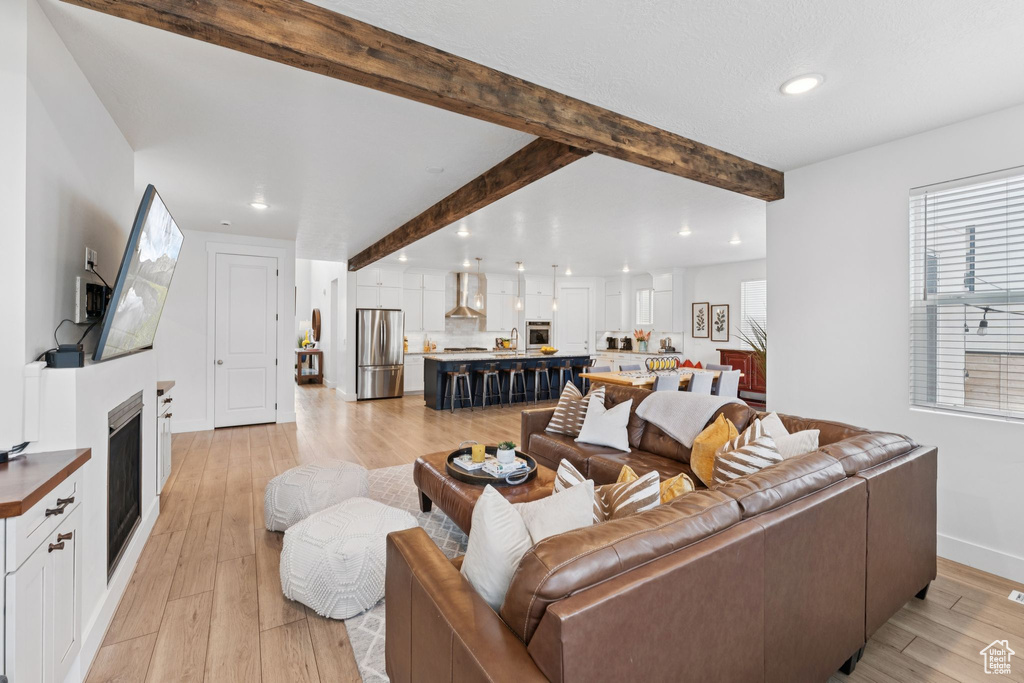 Living area with recessed lighting, beam ceiling, light wood-style flooring, and a fireplace