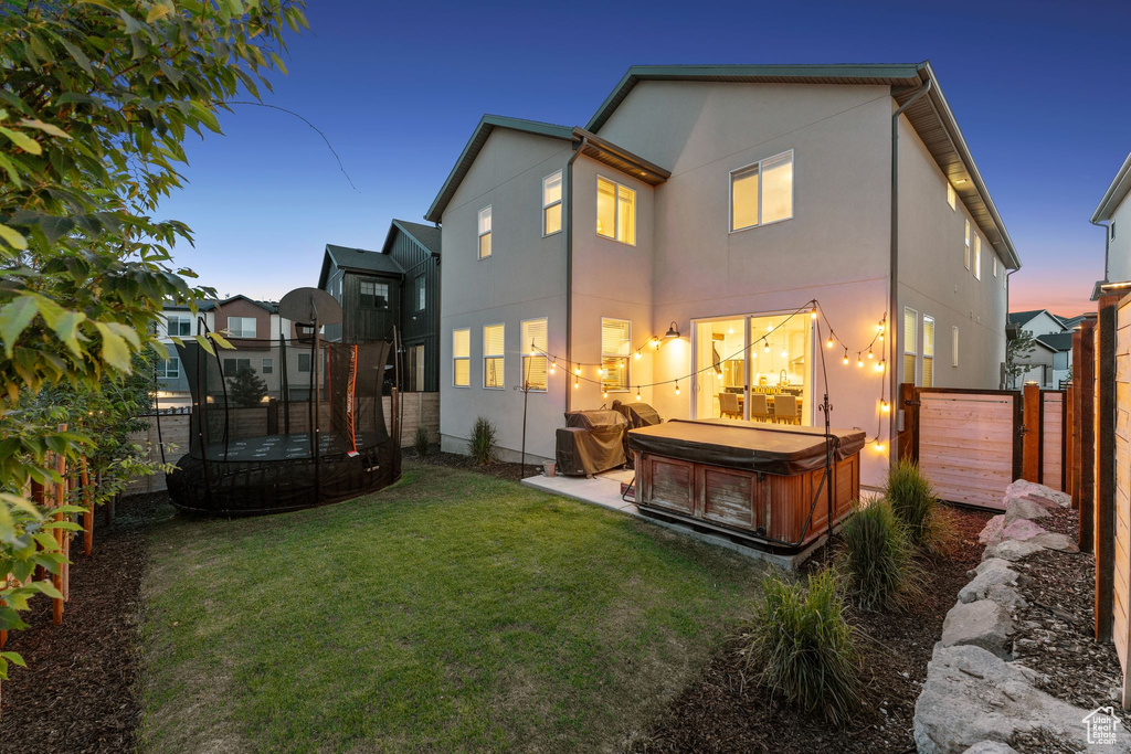 Back of property at dusk with a hot tub, a trampoline, a fenced backyard, and stucco siding