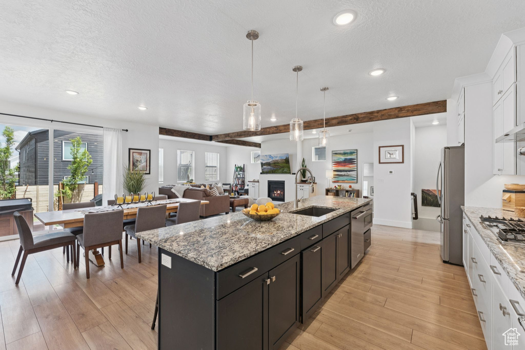 Kitchen featuring stainless steel appliances, white cabinetry, a center island with sink, a textured ceiling, and healthy amount of natural light