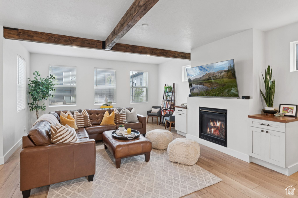 Living room with light wood-type flooring, a glass covered fireplace, beamed ceiling, and plenty of natural light