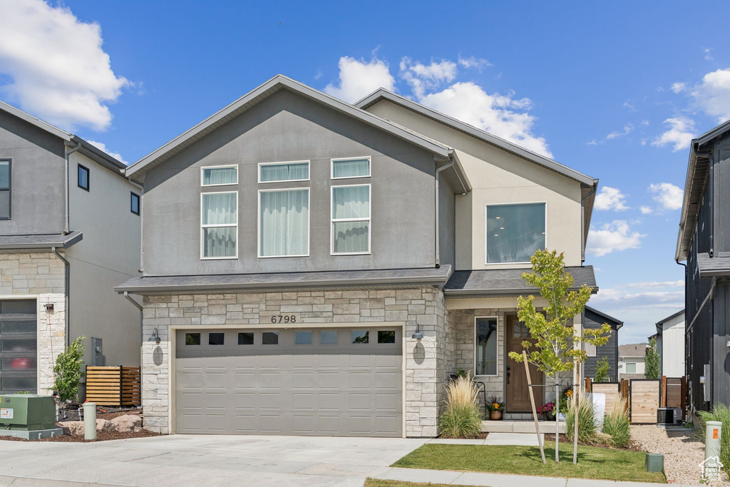 View of front of property featuring stone siding, stucco siding, driveway, and an attached garage