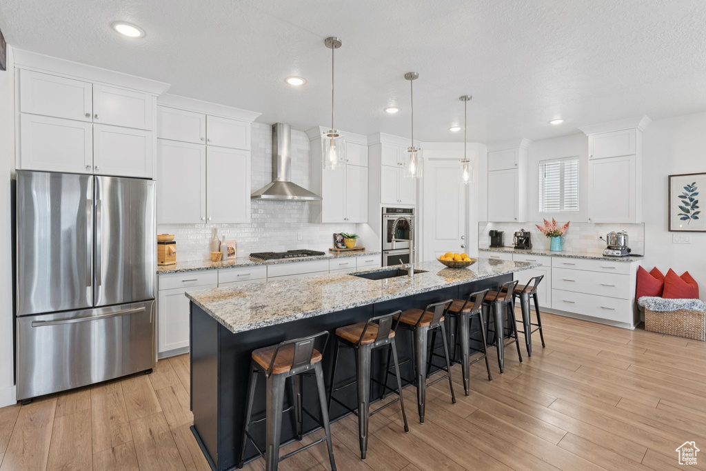 Kitchen with appliances with stainless steel finishes, wall chimney exhaust hood, a breakfast bar, backsplash, and white cabinets
