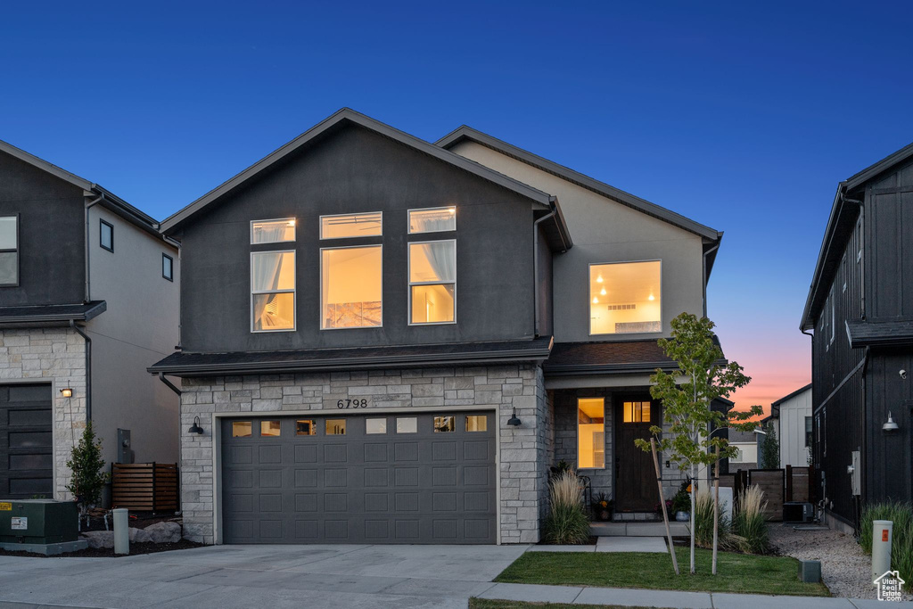 View of front of property with stone siding, a garage, concrete driveway, and stucco siding