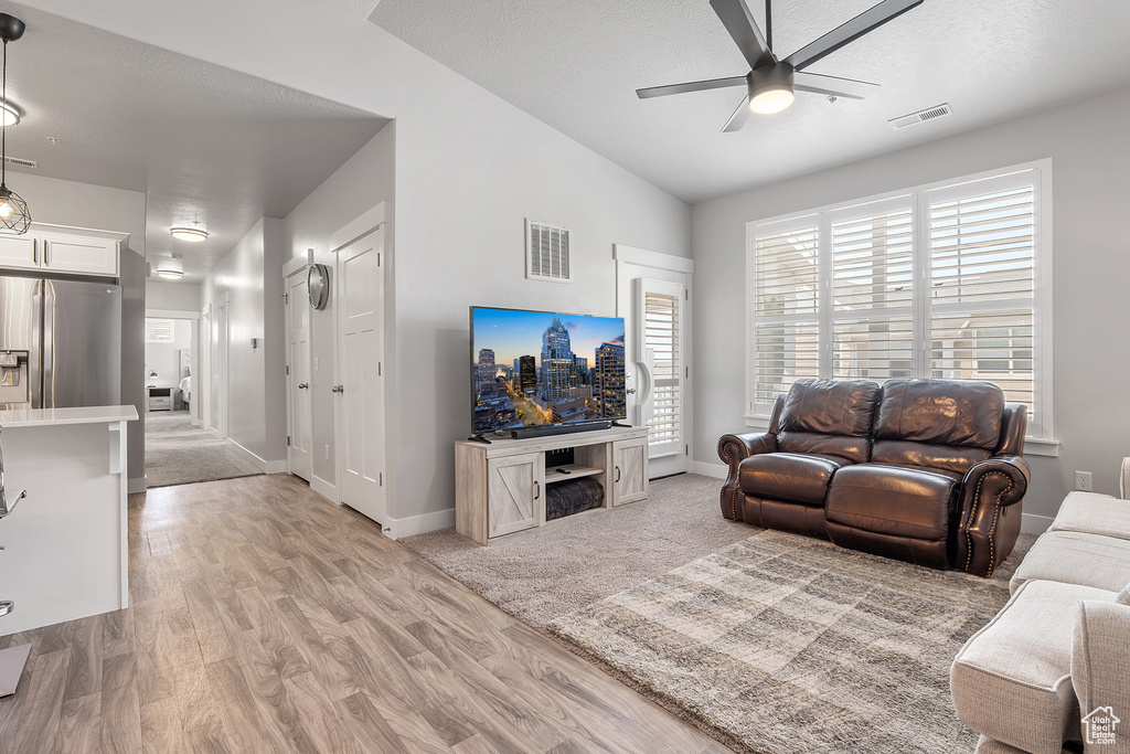 Living area with ceiling fan, light wood-style floors, and vaulted ceiling