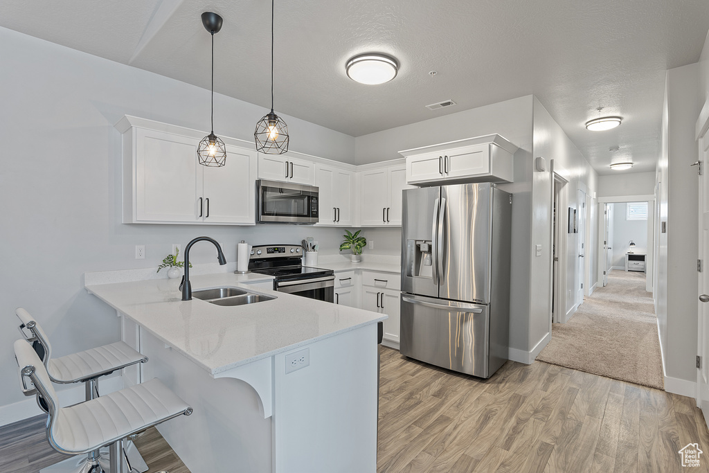 Kitchen with appliances with stainless steel finishes, light countertops, a peninsula, a kitchen breakfast bar, and white cabinets
