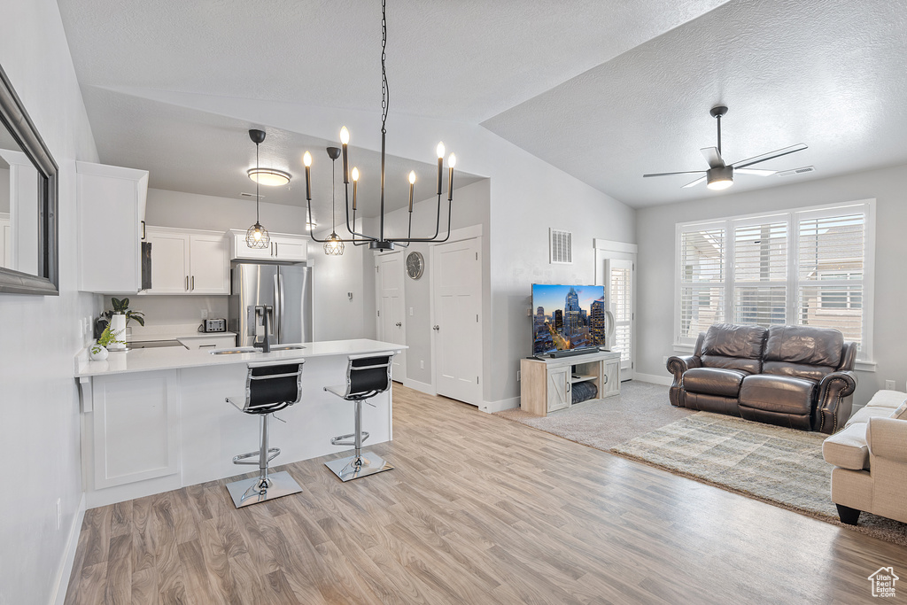 Kitchen with stainless steel fridge with ice dispenser, vaulted ceiling, a peninsula, open floor plan, and light countertops